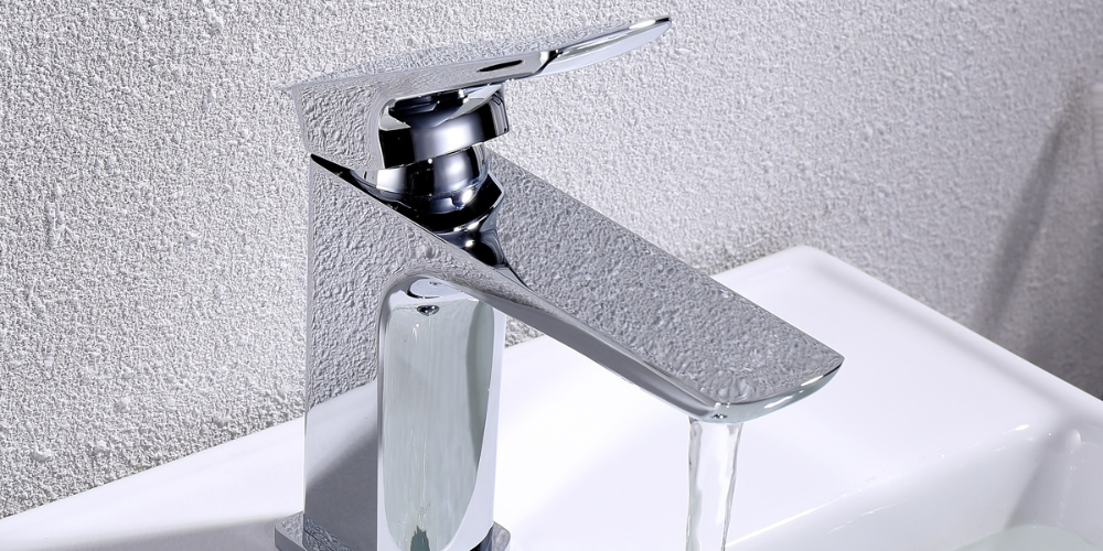 Chrome single-lever faucet releasing water into white sink with textured grey wall tiles in background.