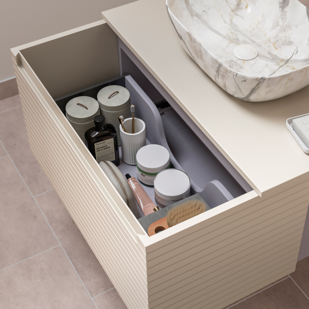 Open cream-colored bathroom drawer with neatly organized jars, bottles, brushes, and toothbrush holder near marble sink.